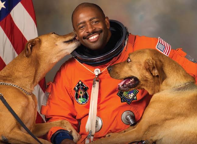 Leland Melvin in his astronaut outfit with his two dogs